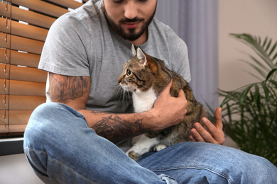 Man with tabby cat near window indoors, closeup. Friendly pet