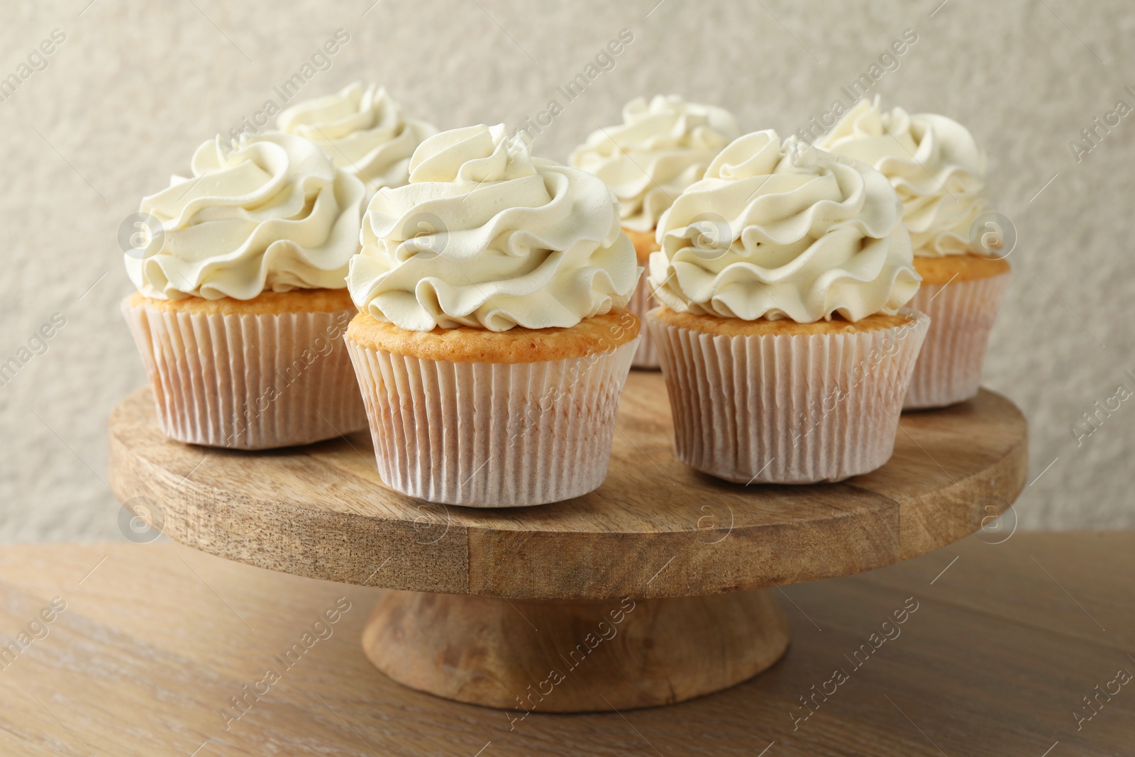 Photo of Tasty vanilla cupcakes with cream on wooden table