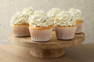 Photo of Tasty vanilla cupcakes with cream on wooden table