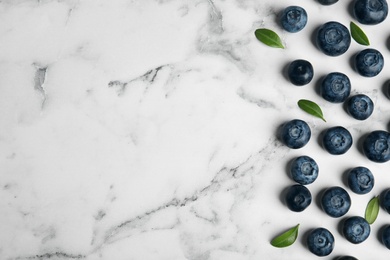 Tasty fresh blueberries and leaves on marble table, flat lay with space for text