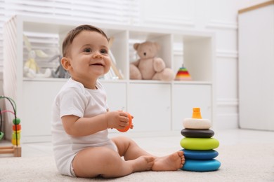Photo of Cute baby boy playing with toy pyramid on floor at home