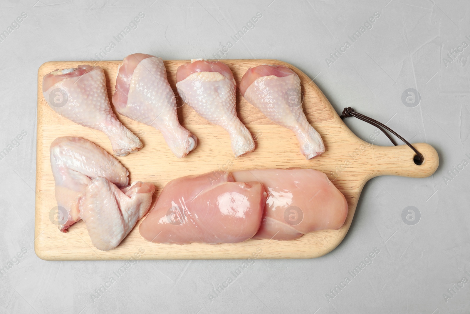 Photo of Wooden board with raw chicken breasts, wings and drumsticks on gray background, top view