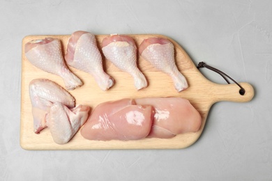 Wooden board with raw chicken breasts, wings and drumsticks on gray background, top view