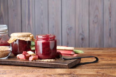 Tasty rhubarb sauce and ingredients on wooden table, space for text