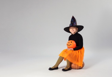 Cute little girl with pumpkin candy bucket wearing Halloween costume on grey background. Space for text