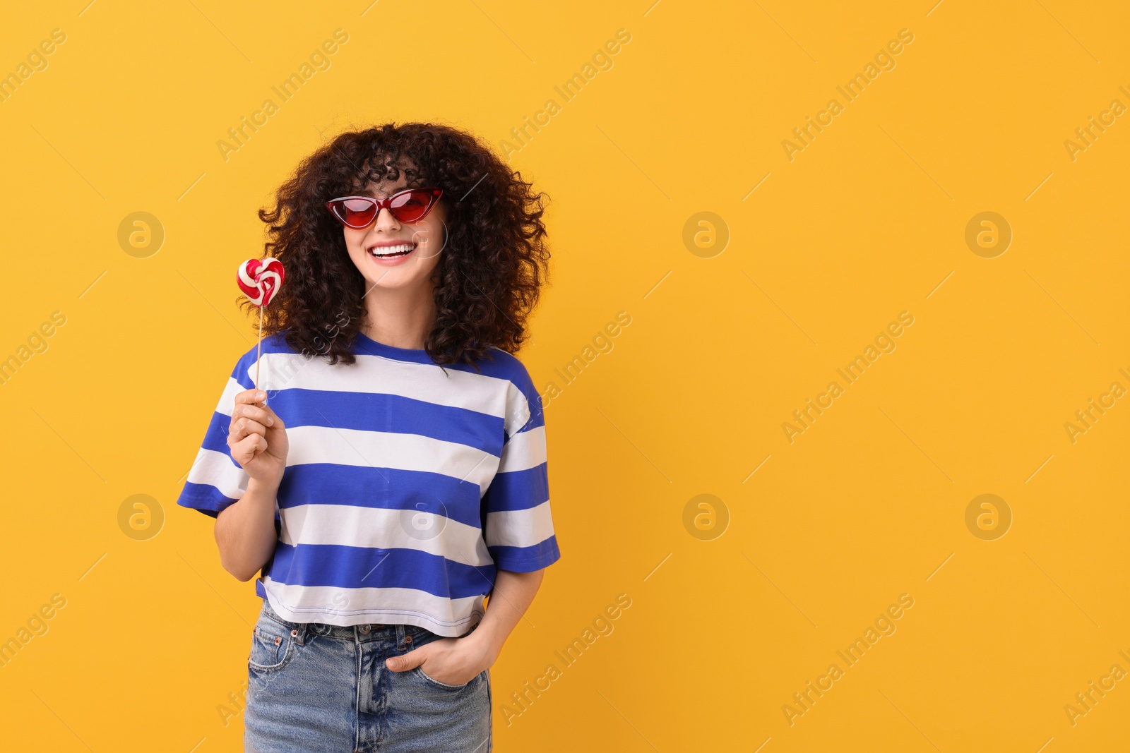 Photo of Beautiful woman in sunglasses with lollipop on yellow background, space for text