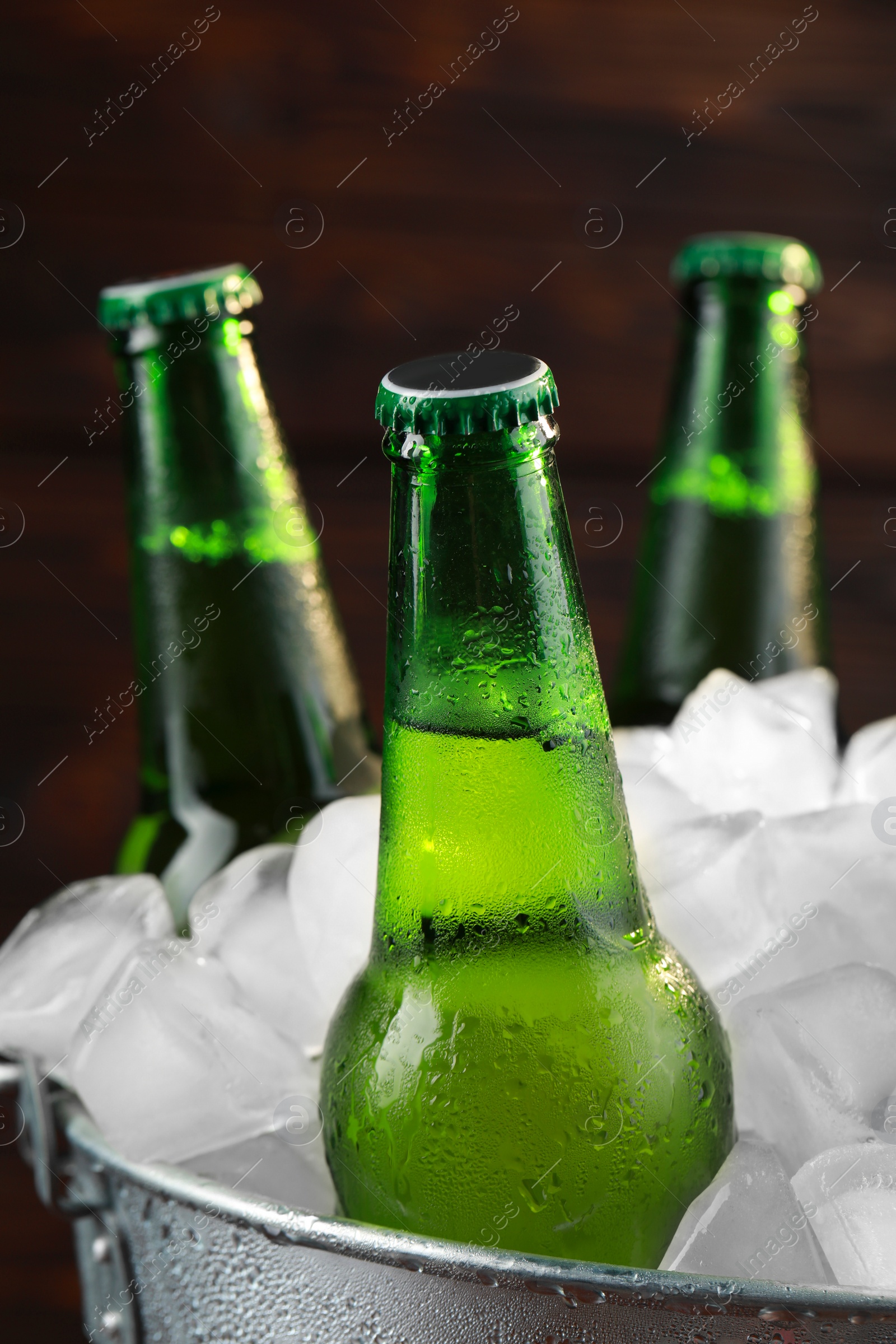 Photo of Metal bucket with bottles of beer and ice cubes on wooden background, closeup