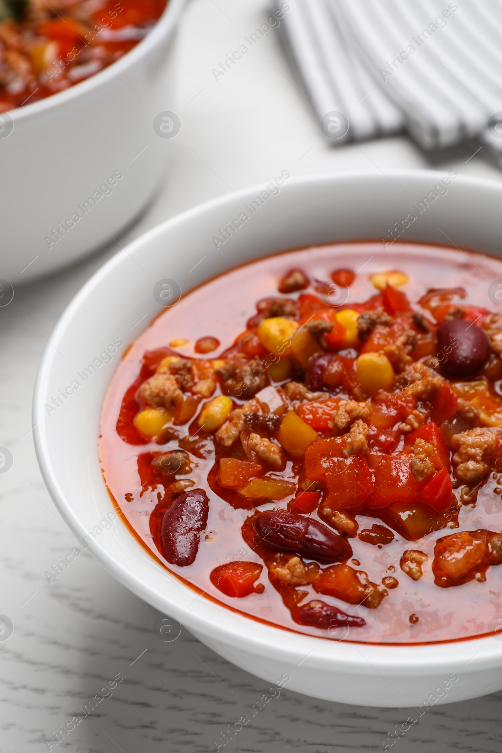 Photo of Bowl with tasty chili con carne on white wooden table, closeup