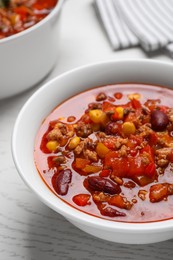 Bowl with tasty chili con carne on white wooden table, closeup