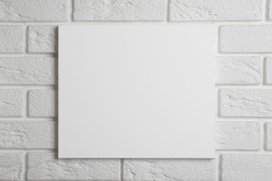 Photo of Blank canvas hanging on white brick wall, space for text