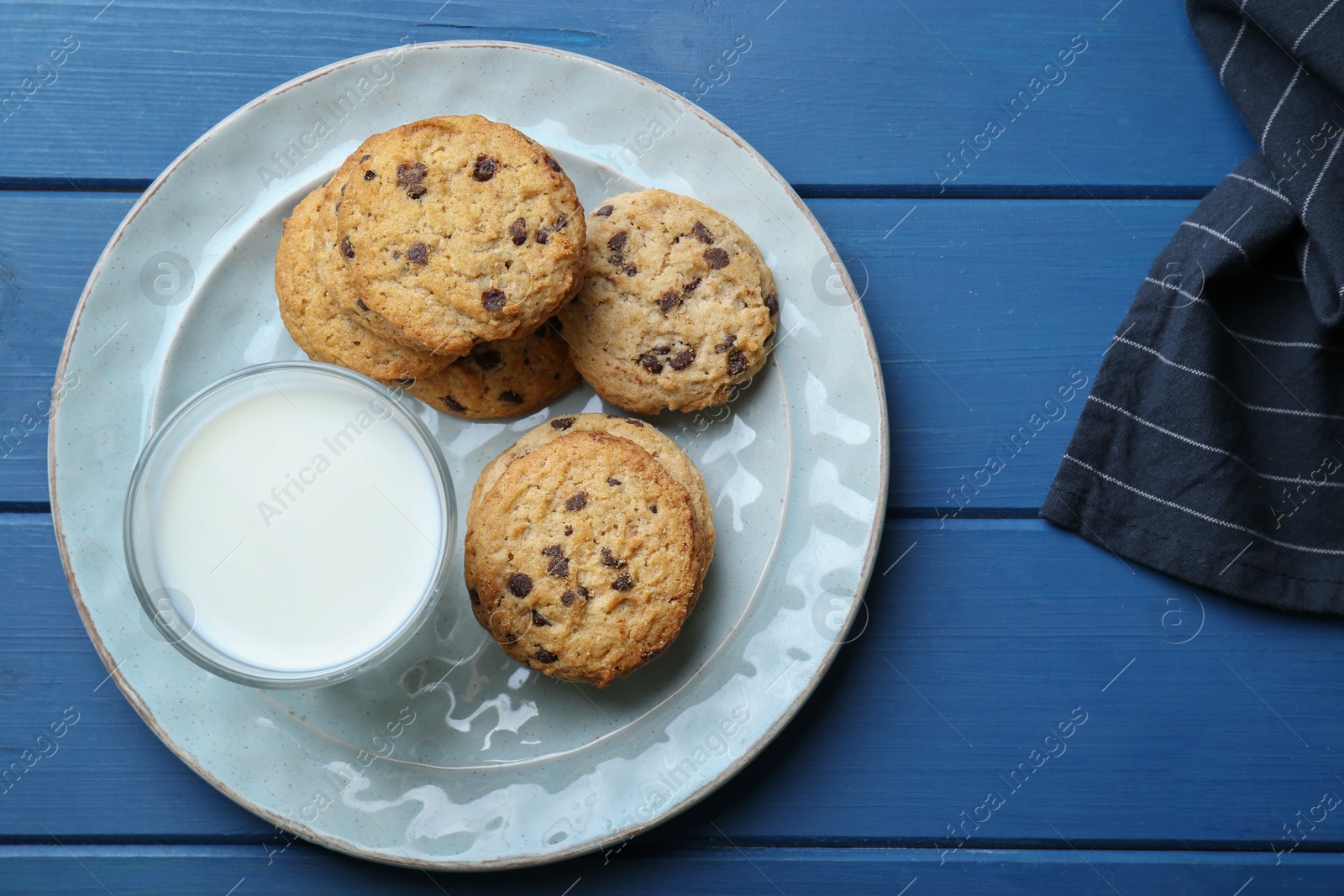 Photo of Tasty chocolate chip cookies and glass of milk on blue wooden table, flat lay