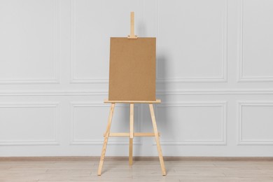 Wooden easel with blank board near white wall indoors