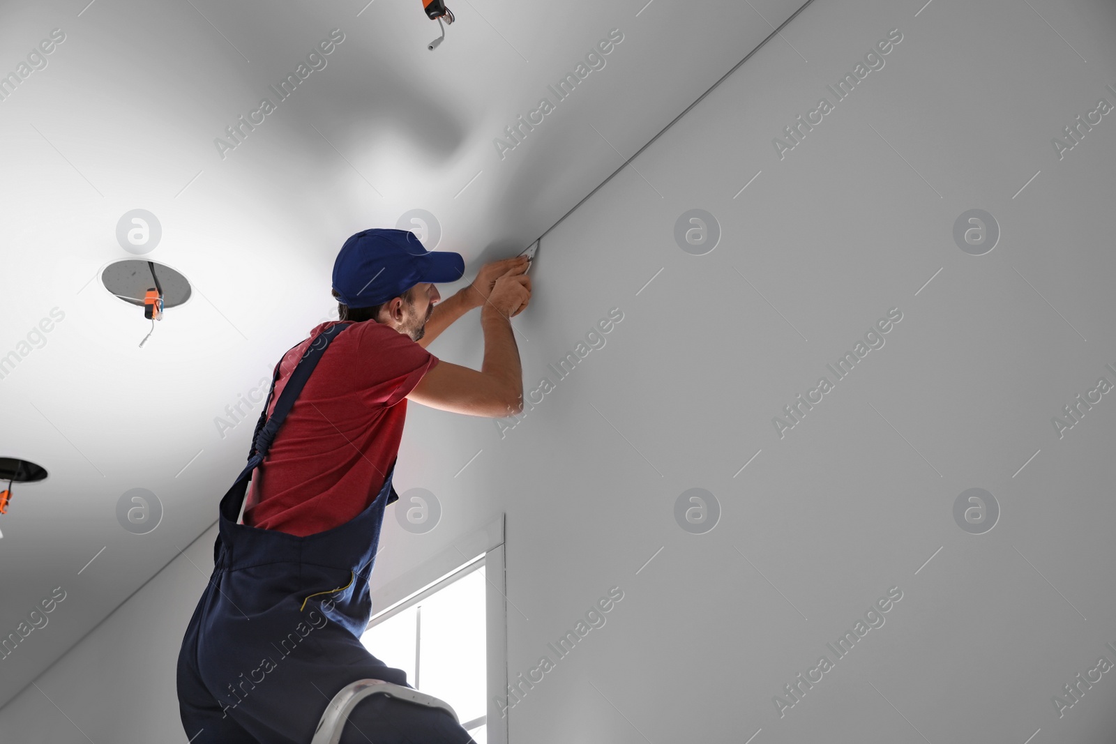 Photo of Worker installing stretch ceiling in empty room. Space for text