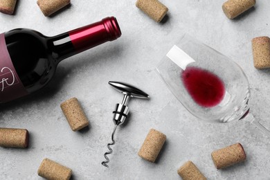 Photo of Corkscrew with wine bottle, glass and stoppers on light grey stone table, flat lay