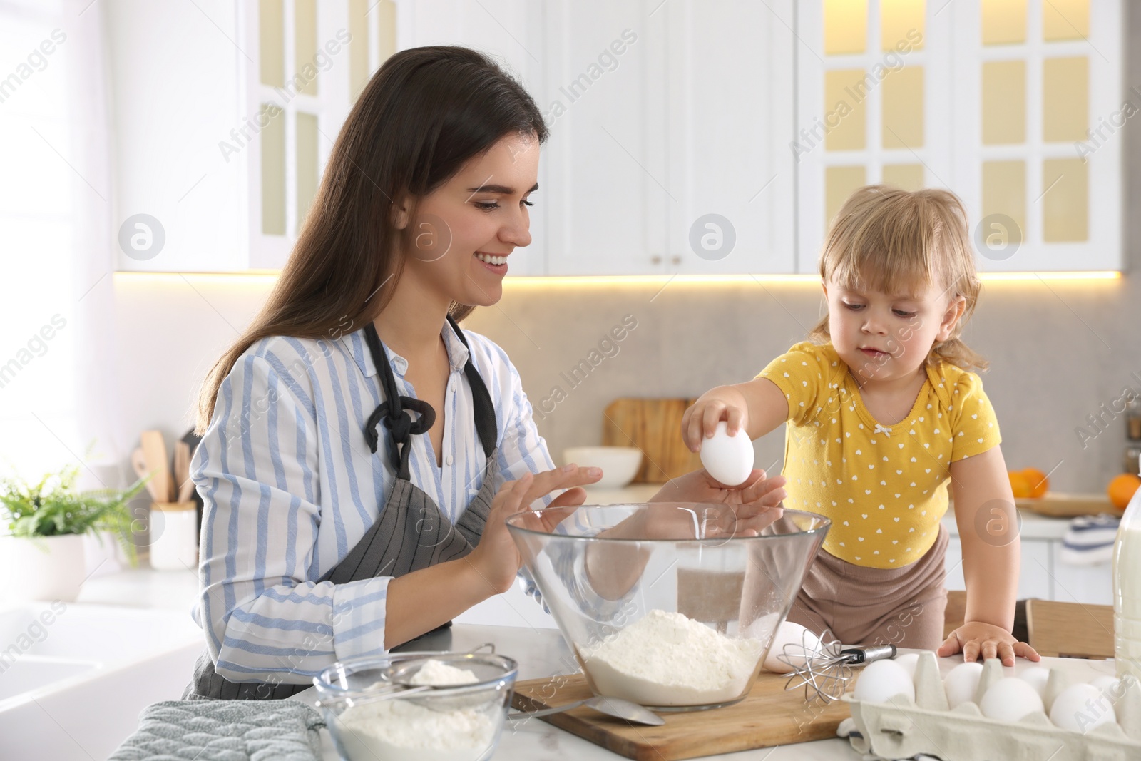 Photo of Mother and her little daughter cooking dough together in kitchen