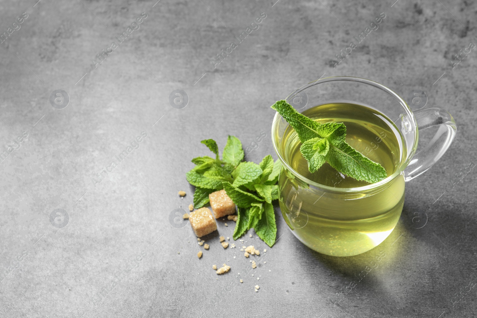 Photo of Cup with hot aromatic mint tea, fresh leaves and sugar cubes on table