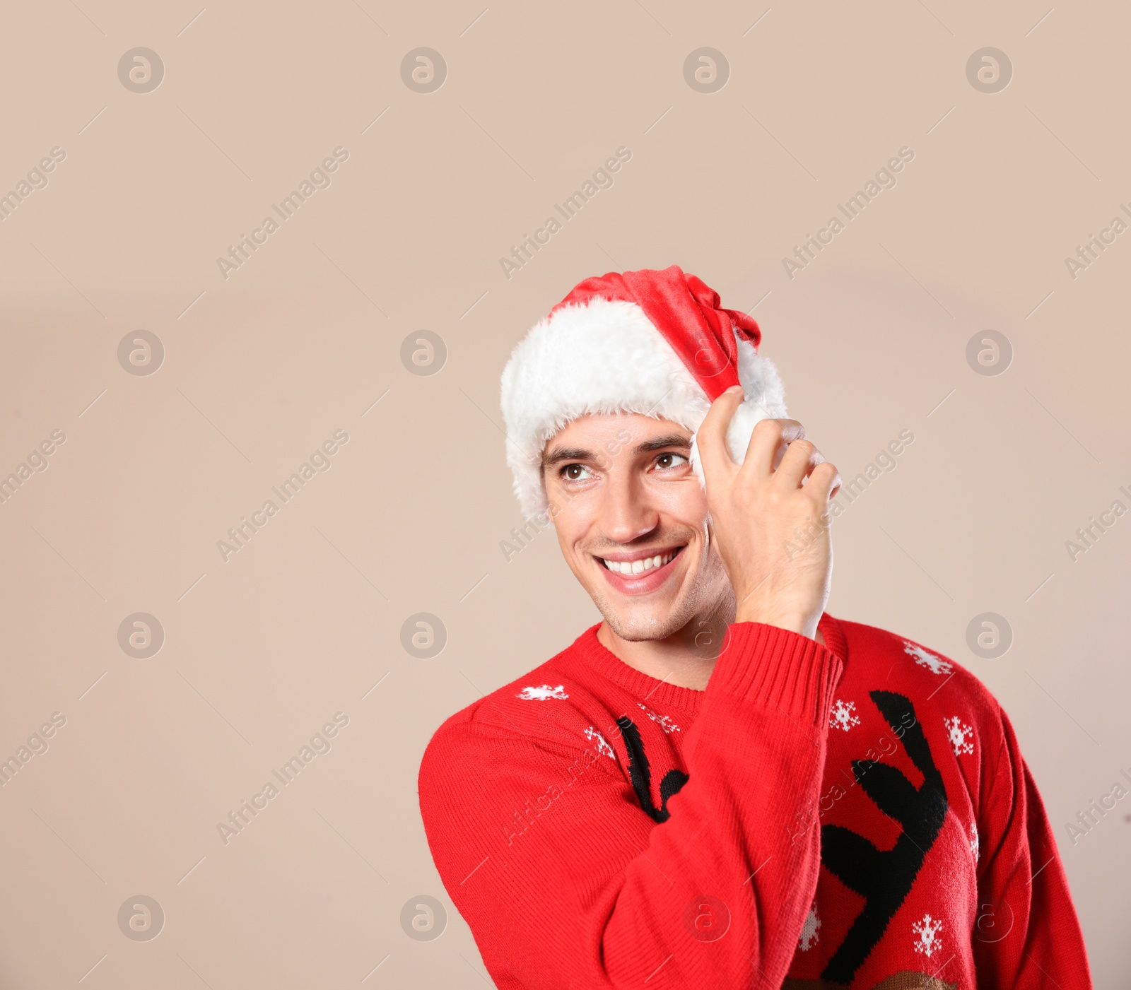 Photo of Portrait of young man in Christmas sweater and Santa hat on beige background