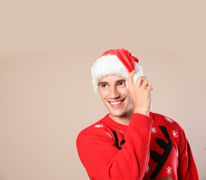 Portrait of young man in Christmas sweater and Santa hat on beige background