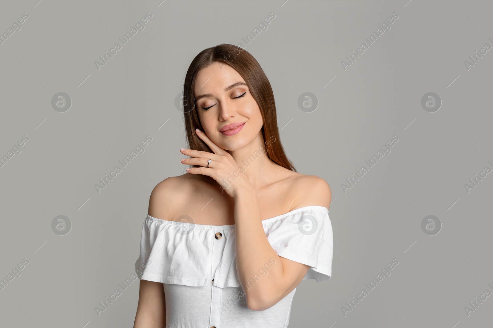 Photo of Happy young woman wearing beautiful engagement ring on grey background