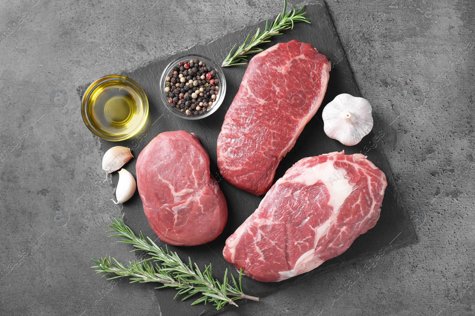 Photo of Raw beef steaks, oil and spices on grey background, top view