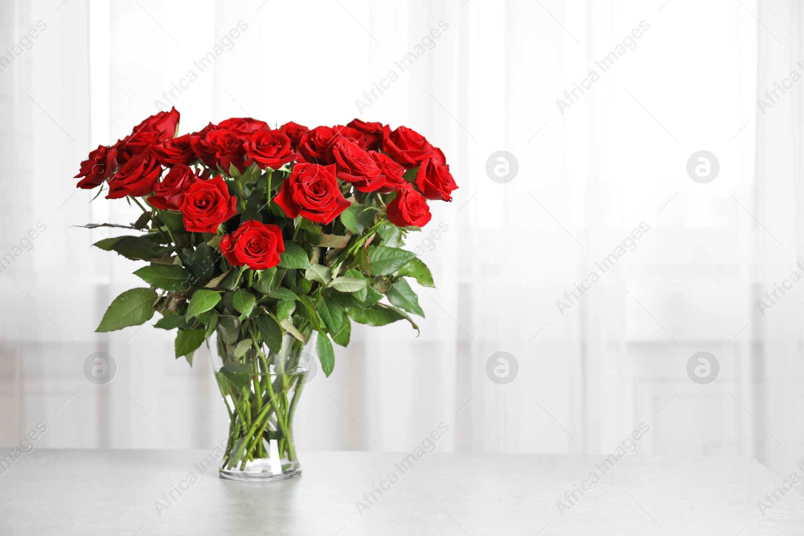 Photo of Vase with beautiful red roses on table against window