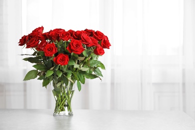 Photo of Vase with beautiful red roses on table against window