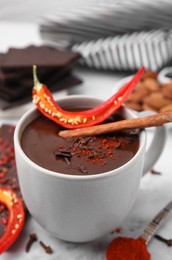 Photo of Cup of hot chocolate with chili pepper and cinnamon on white marble table, closeup