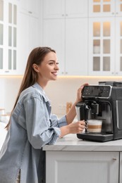 Photo of Young woman preparing fresh aromatic coffee with modern machine in kitchen