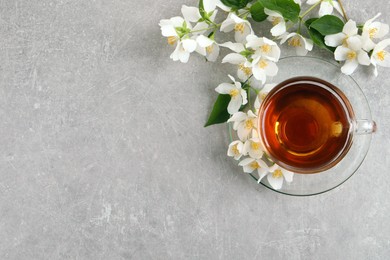 Photo of Glass cup of aromatic jasmine tea and fresh flowers on grey table, flat lay. Space for text