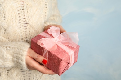 Young woman holding Christmas gift on blue background, closeup