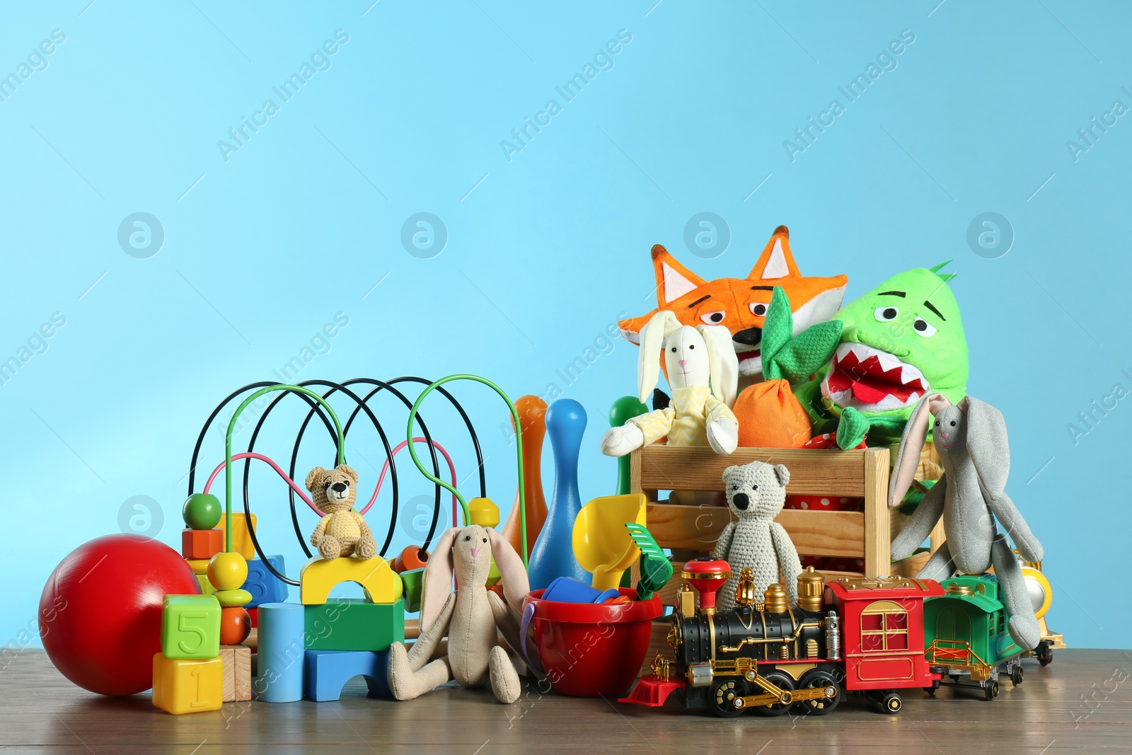 Photo of Many different toys on wooden table against light blue background