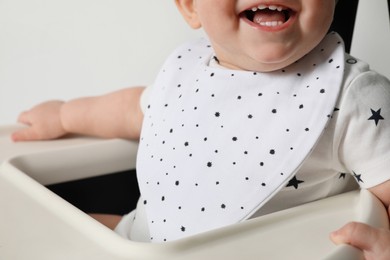 Photo of Cute little baby wearing bib in highchair on white background, closeup