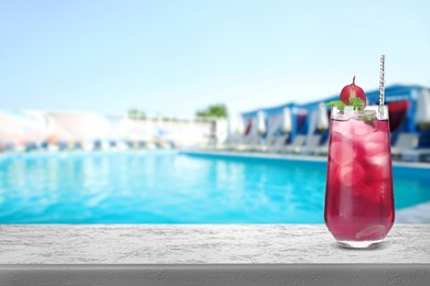 Image of Tasty refreshing cocktail on light grey stone table near outdoor swimming pool, space for text