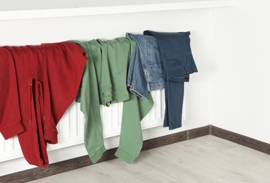 Clean clothes hanging on white radiator in room