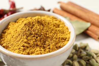 Photo of Curry powder in bowl and other spices on table, closeup