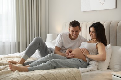 Photo of Young pregnant woman with her husband in bedroom