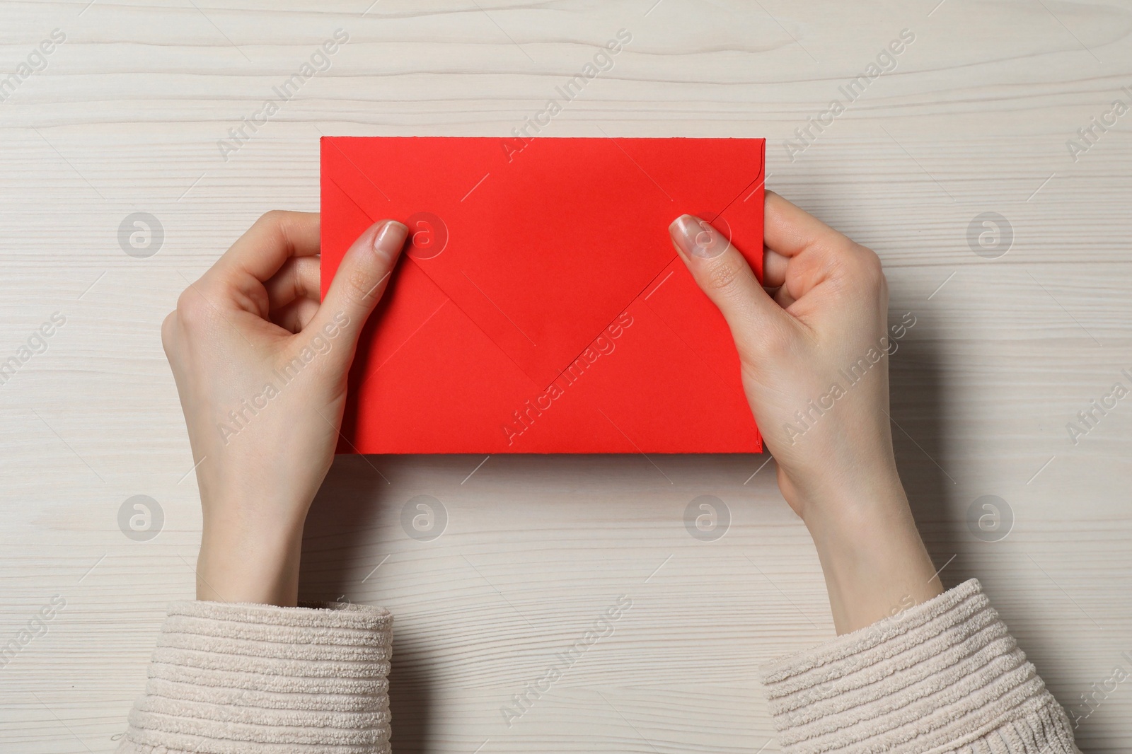 Photo of Woman with red letter envelope at light wooden table, top view. Space for text