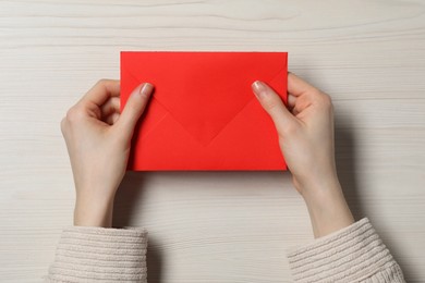 Woman with red letter envelope at light wooden table, top view. Space for text