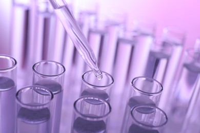 Photo of Dripping liquid from pipette into test tube on violet background, closeup