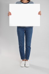 Photo of Woman holding blank poster on light grey background, closeup