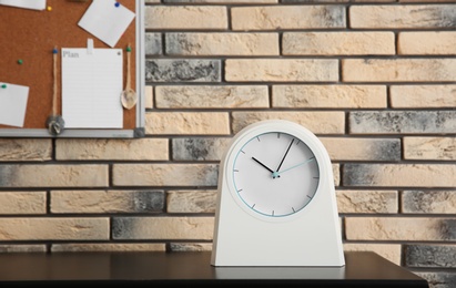Stylish clock on table near brick wall. Time management