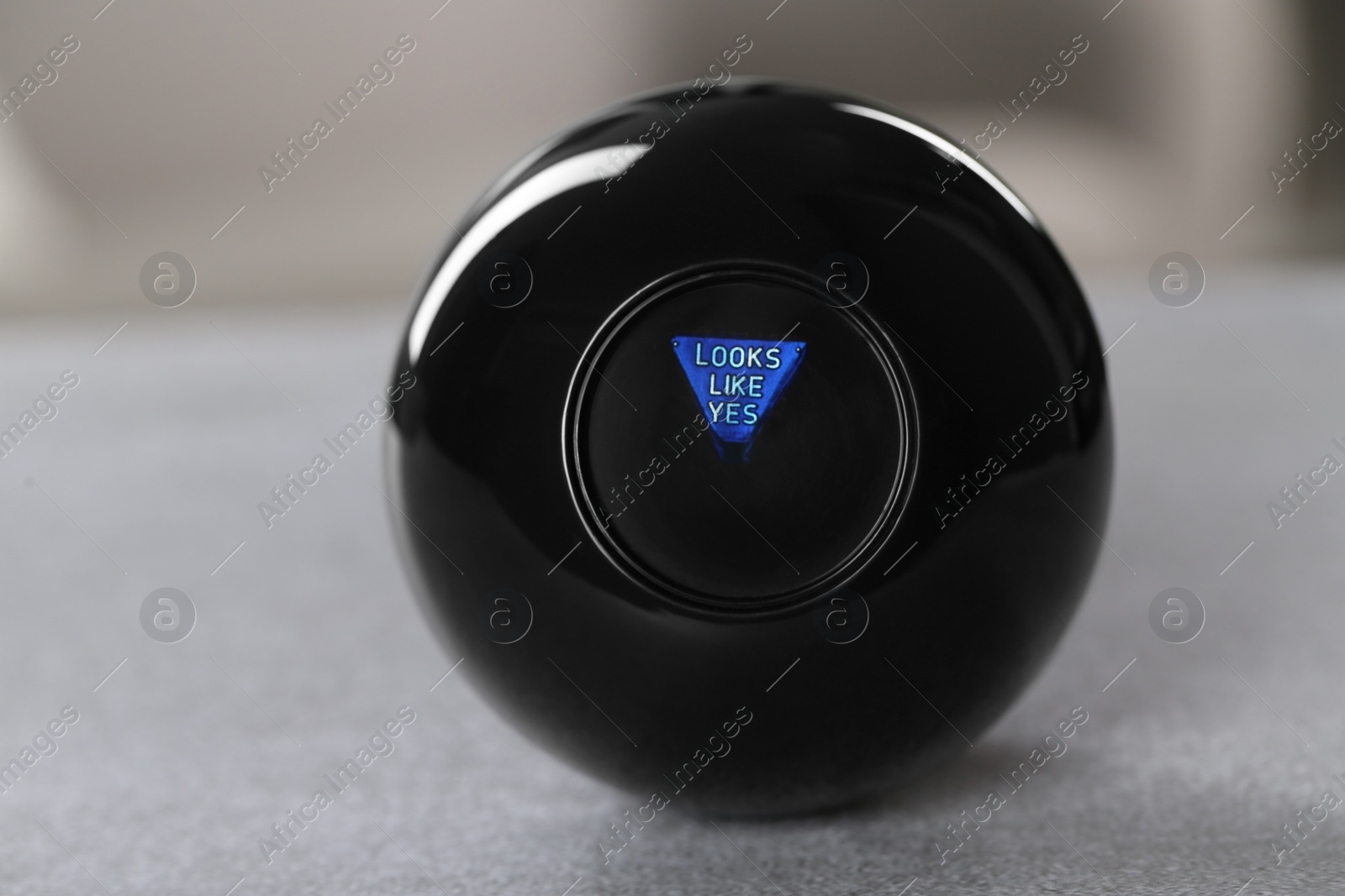 Photo of Magic eight ball with prediction Looks Like Yes on light gray table, closeup