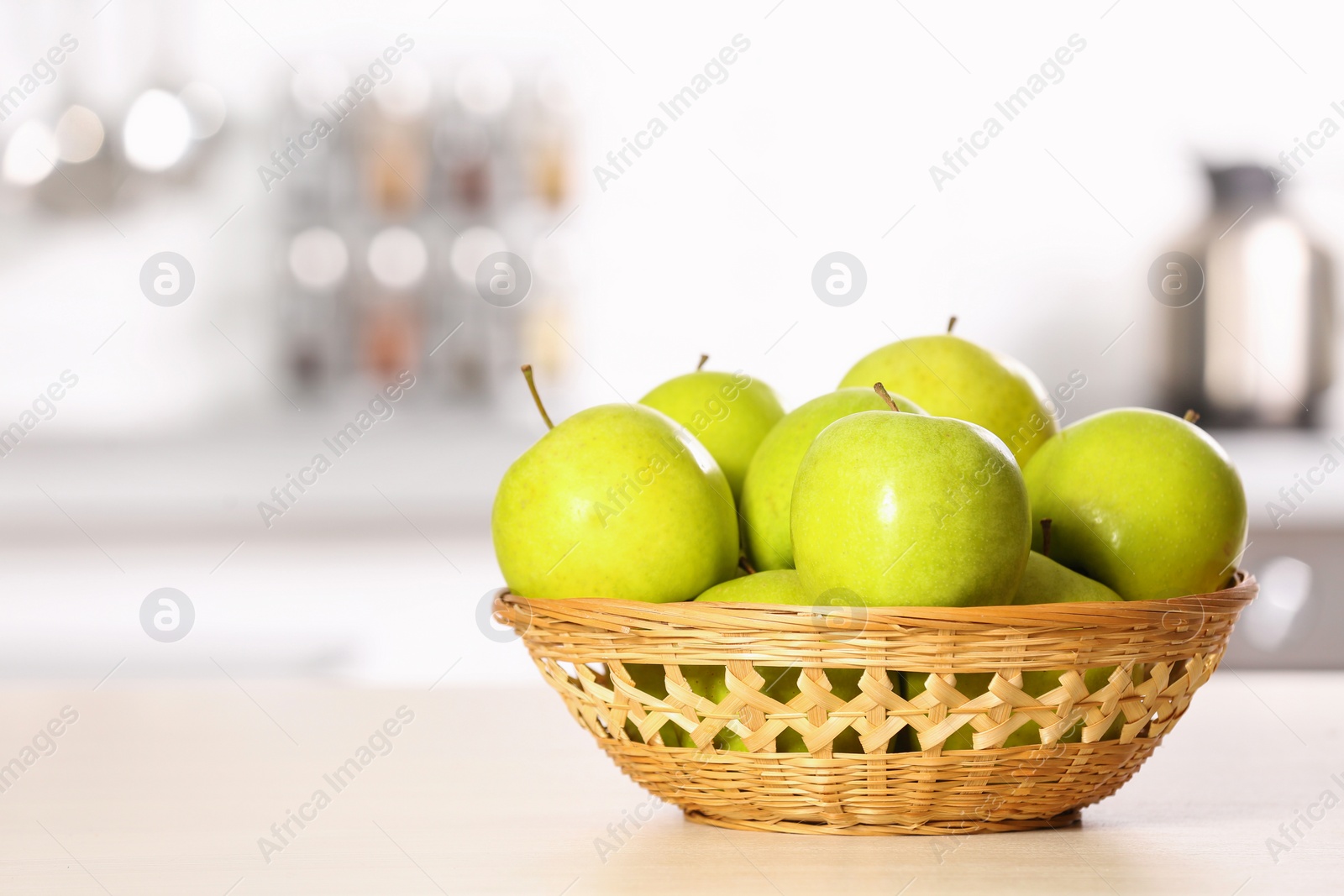 Photo of Wicker bowl with sweet green apples on table in kitchen, space for text