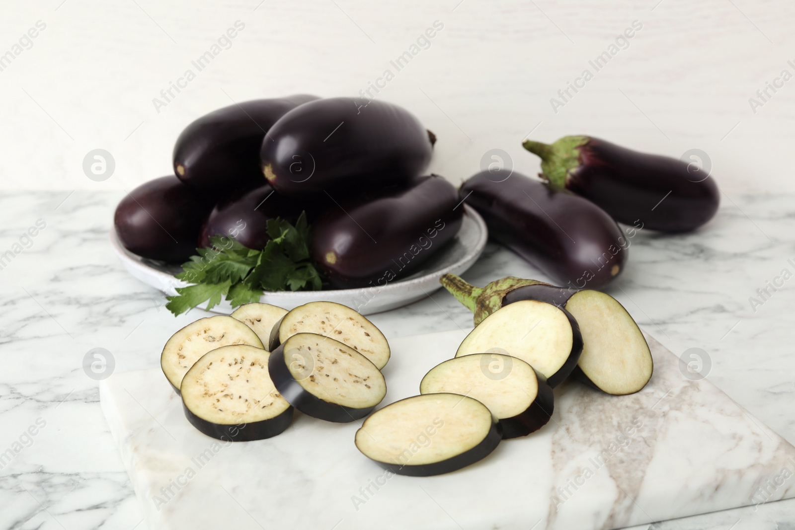 Photo of Cut and whole raw ripe eggplants on white marble table