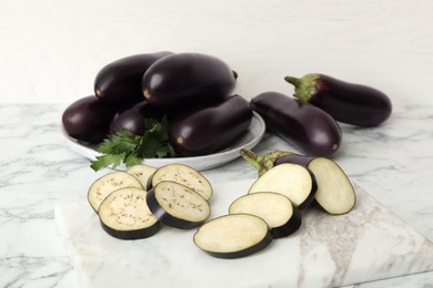 Cut and whole raw ripe eggplants on white marble table