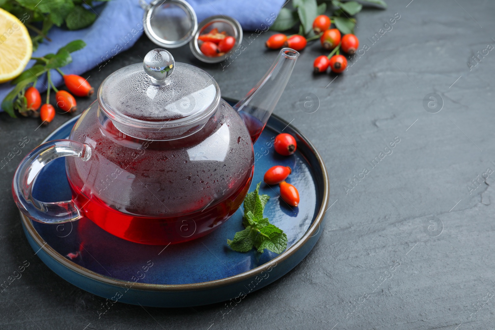 Photo of Teapot with aromatic rose hip tea, berries and mint on black table, space for text