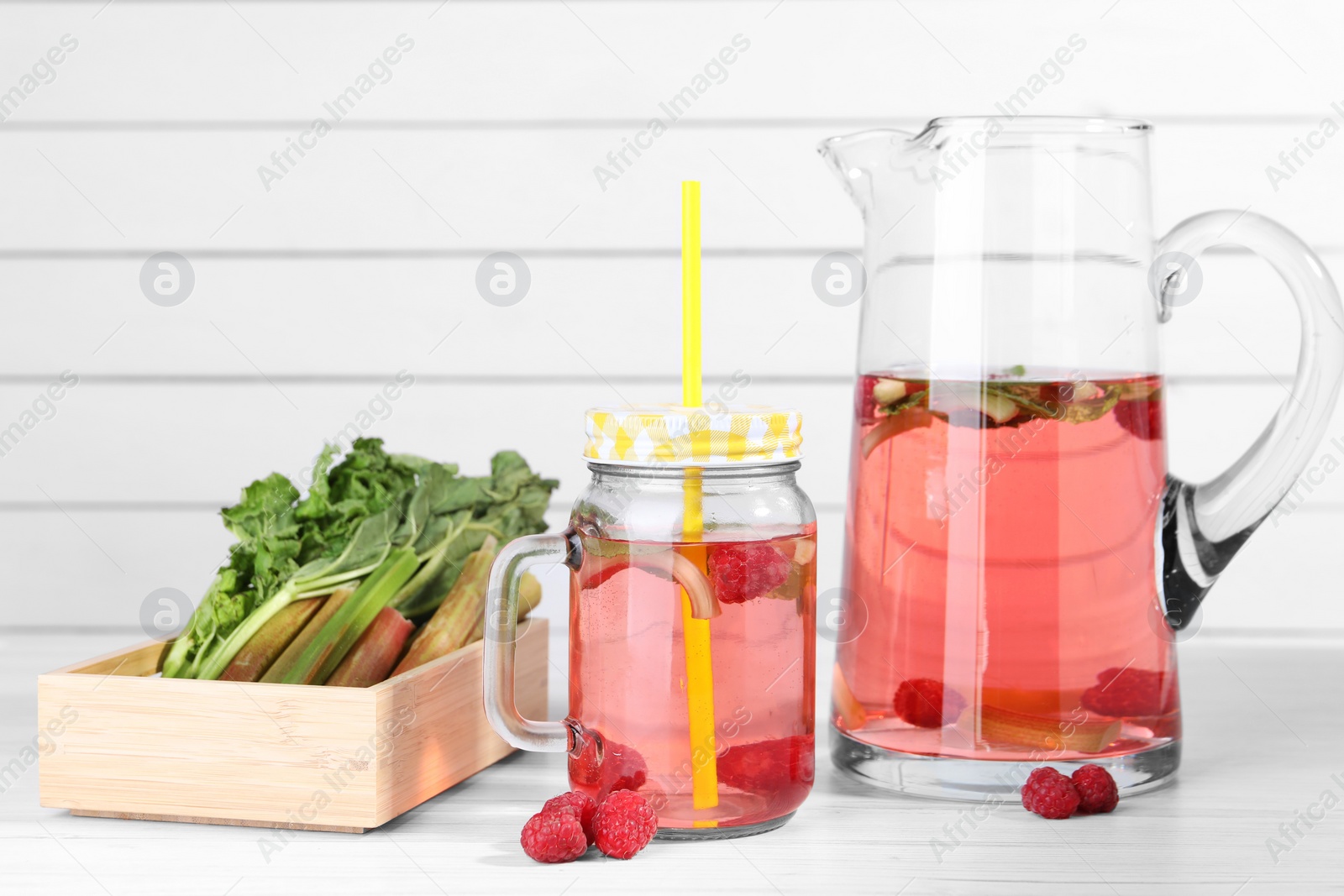 Photo of Tasty rhubarb cocktail with raspberry and stalks on white wooden table