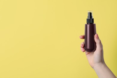 Woman holding spray bottle with hair thermal protection against pale yellow background, closeup. Space for text