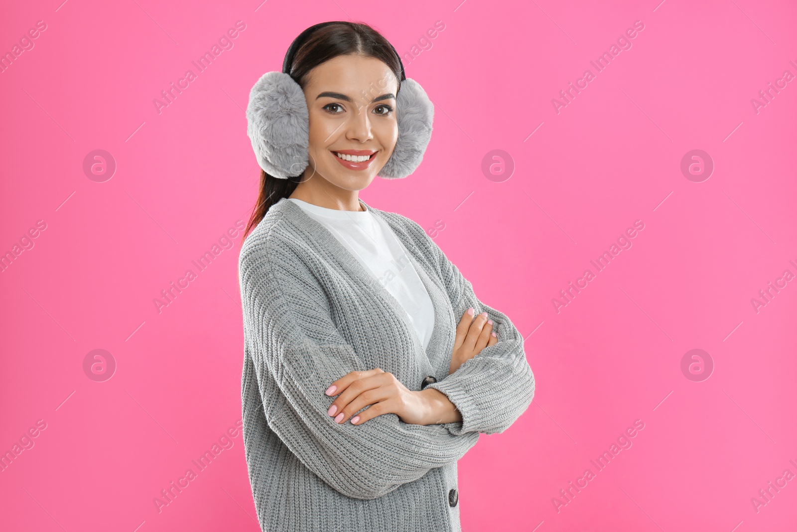 Photo of Beautiful young woman wearing earmuffs on pink background