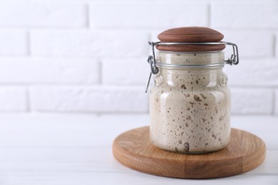 Photo of Sourdough starter in glass jar on white wooden table, space for text